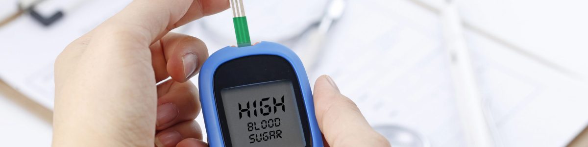 Hand holding a blood glucose meter measuring blood sugar, the background is a stethoscope and chart file